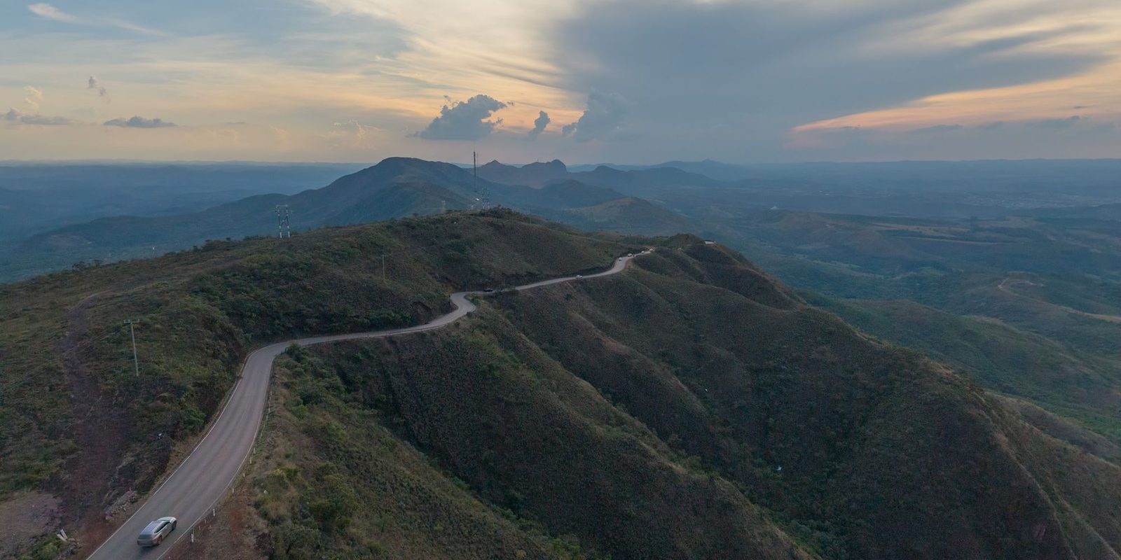Estrada sinuosa no alto de uma serra de Minas Gerais ao entardecer, com um carro subindo a pista